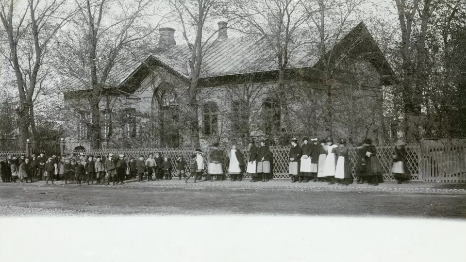 Black and white photo of a large group of small children in front of a building. Photo. 