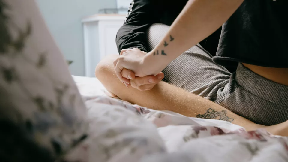 A couple sit on a bed holding hands.
