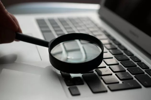 A magnifying glass lies on a laptop's keyboard. Photo: Unsplash, Agence Olloweb.