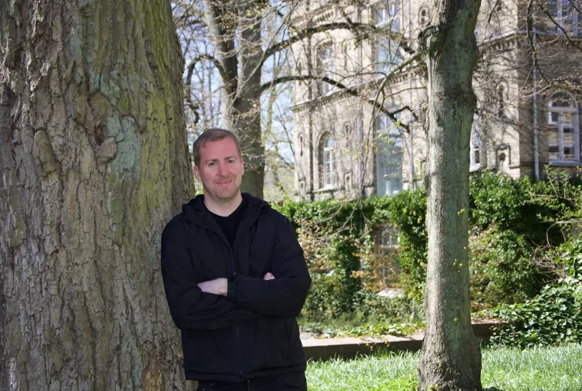 Portrait of Colm Flaherty leaning against a tree. Photo: Emma Lord. 