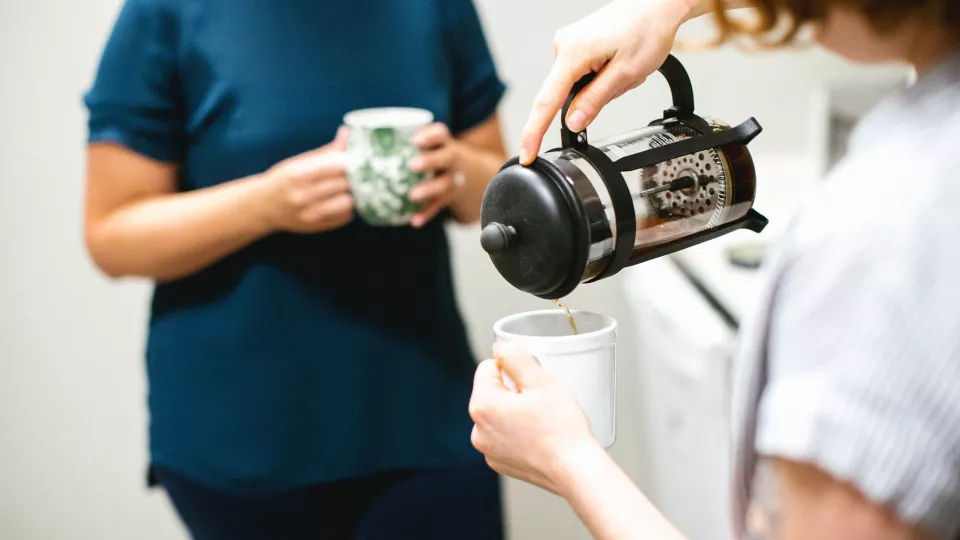 One person with a coffee cup, another person pouring coffee. Photo: Unsplash. 