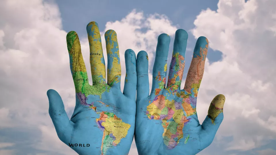 The world map painted onto a pair pf hands with the sky in the background. Photo: Pixabay. 