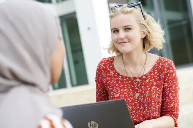 Kvinna i blommig röd top och solgalsögon med laptop. Foto.