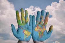 The world map painted onto a pair pf hands with the sky in the background. Photo: Pixabay. 