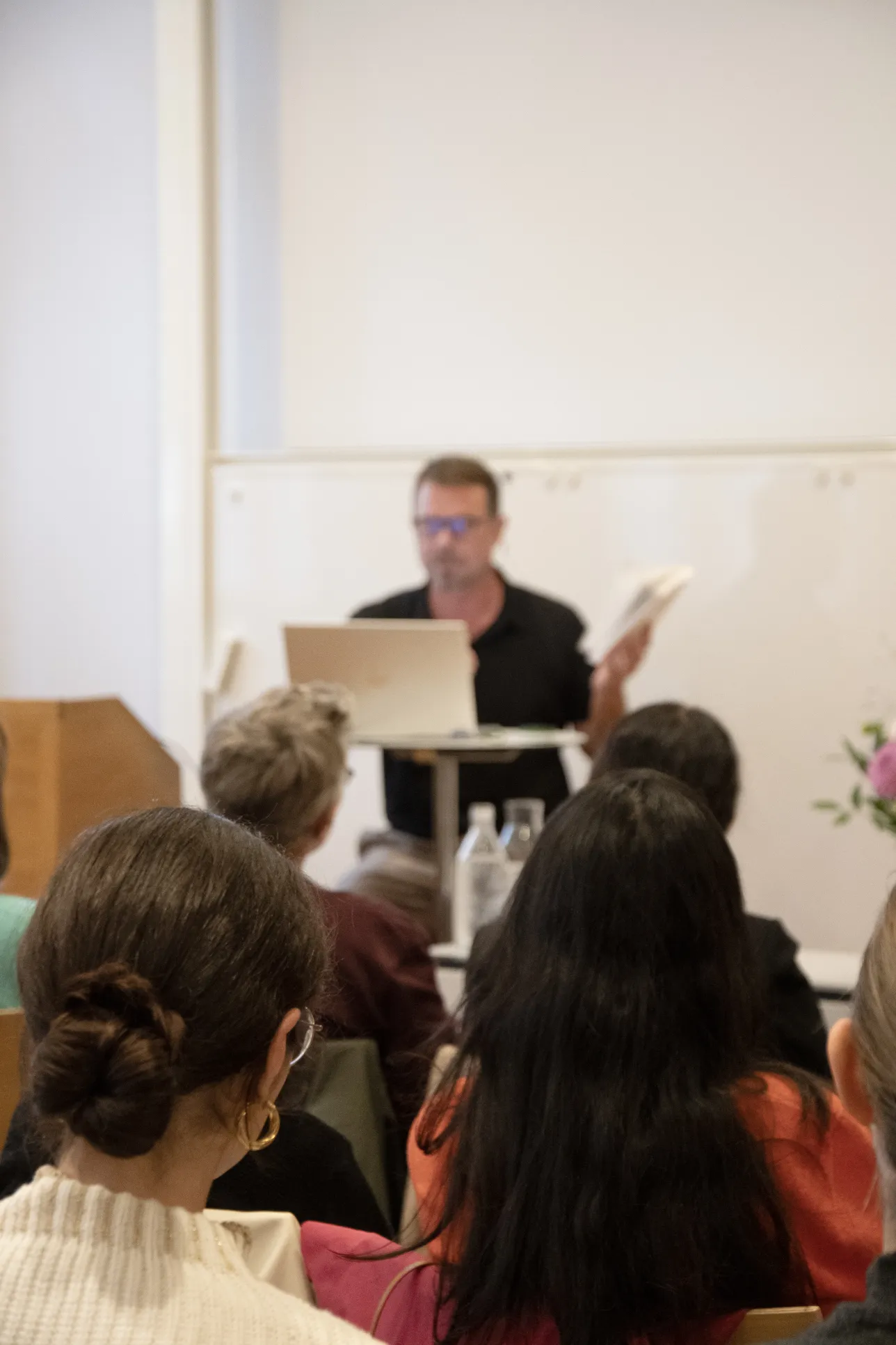 Publiken huvuden syns bakifrån. Anders Burman syns suddigt i bakgrunden. Foto: Emma Lord. 