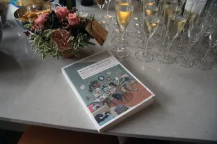 Avhandling i bokform på ett bord med glas och blommor.